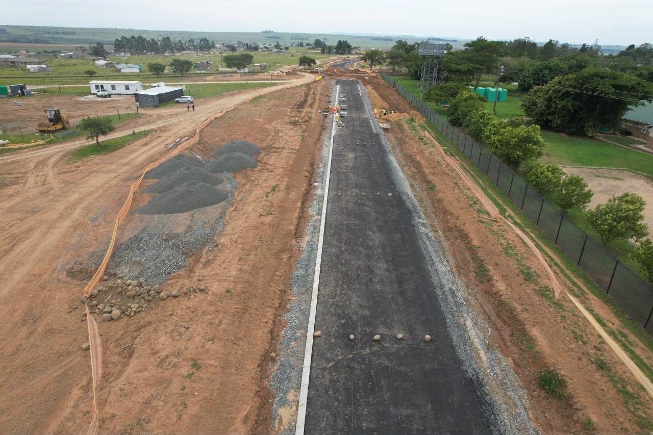 New asphalt road under construction with kerb, stone stockpiles and site offices